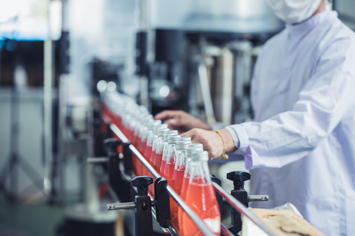 A drink factory worker beside a conveyor belt of bottled products in a production facility with water treatment