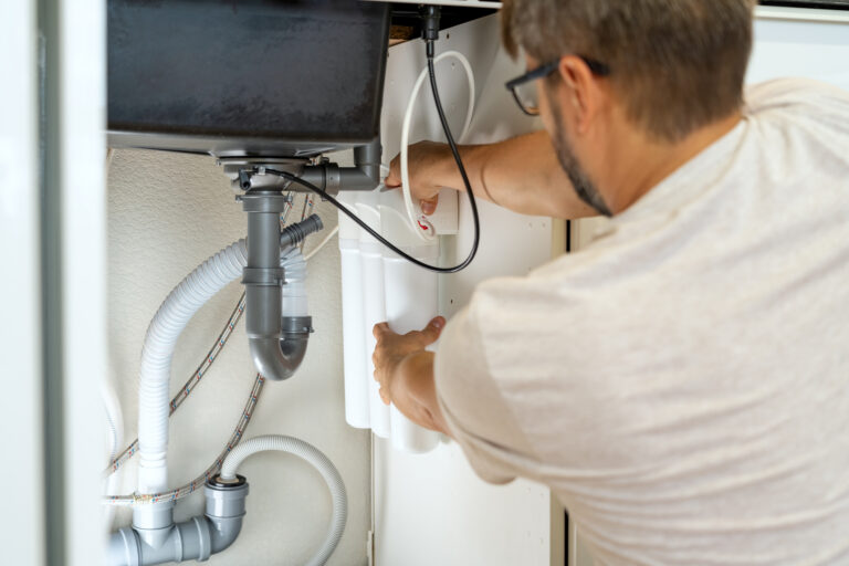 Plumber installs water filter and changes water filter cartridges in kitchen under kitchen sink